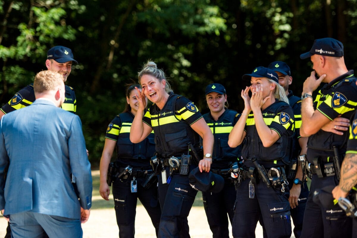 Vrouwelijke verwarmend in uniform lachen buiten in een groene parkachtige omgeving tijdens daglicht, met een man in pak op de voorgrond, rug naar camera. Netwerkevenement voor de politie.