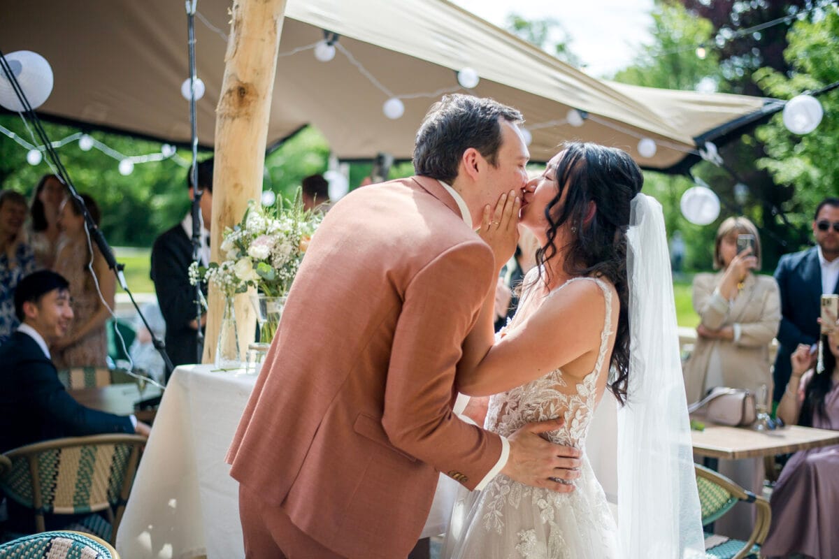 Bruid in kanten trouwjurk kust bruid in lichtbruin pak tijdens romantische bruiloft Nienoord; buitenfeest met sfeerverlichting, gedecoreerde tafel en feestelijke gasten.