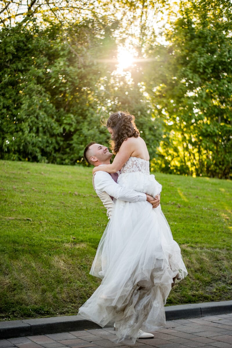 Bruid en bruidegom op buitenlocatie Garnwerd aan Zee, onderaan door groen gras en bomen, romantische bruiloftssfeer met zonlicht op geplaveid tuinpad.