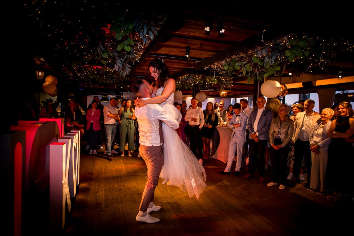 Bruid en bruiloft dansen tijdens bruiloft in Garnwerd aan Zee, omringd door feestelijke gasten en verlichte LOVE-letters op de dansvloer. Romantische trouwlocatie sfeer.