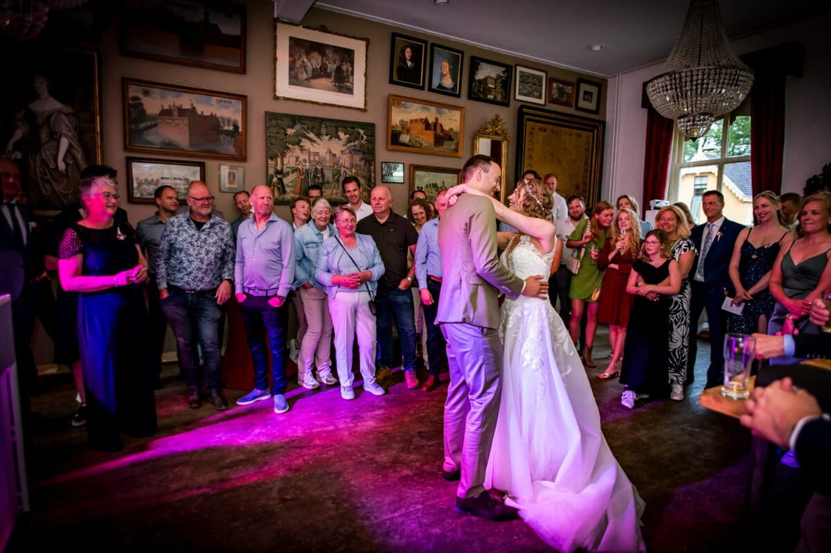 Romantische bruiloftsdans bij Trouwen bij Nienoord, warm verlichte zaal, lachende gasten, roze sfeerverlichting en kroonluchter.
