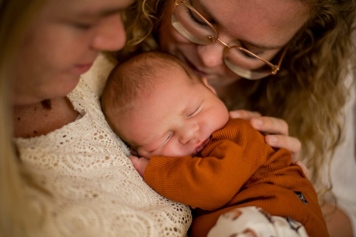 Lichtharige ouders knuffelen een pasgeboren baby in rustgevende kleding die vredig slaapt; intiem, liefdevol familiemoment.