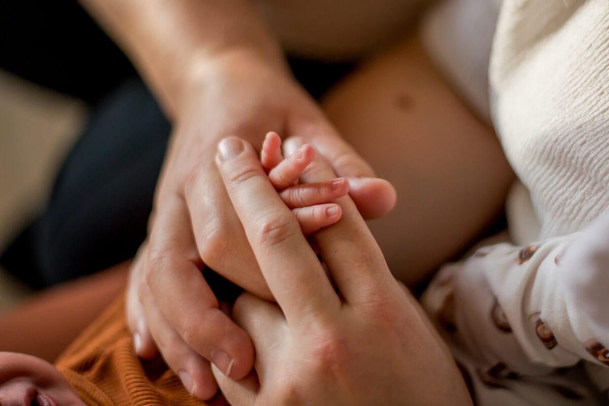 Close-up van volwassen handen die voorzichtig een pasgeboren babyhandje vasthouden, met warmte en tederheid.