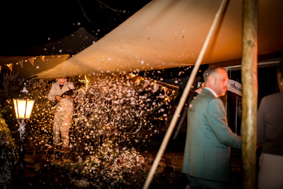 Feestelijk buitenevenement 's nachts met violist in lichtpak onder tent, koordverlichting, vlaggetjes, vallende nepsneeuw en warme gloeilamp.